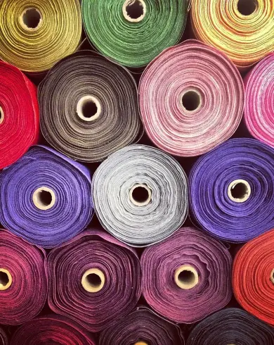 Canlı renklerde, üst üste istiflenmiş çok sayıda tekstil ve kumaş rulosu.